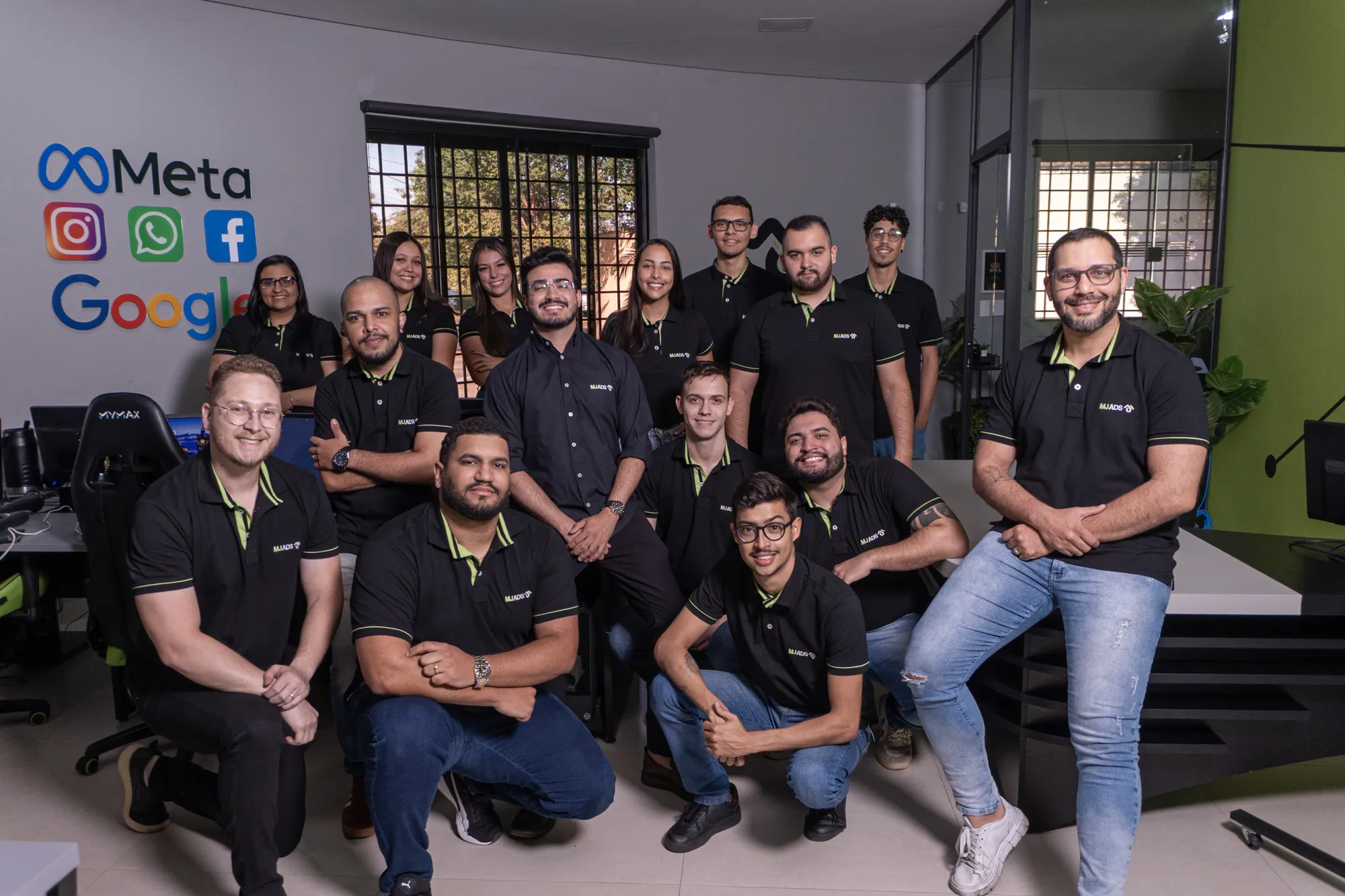 Equipe da MJ ADS reunida no escritório da agência, todos com camisa polo preta da marca